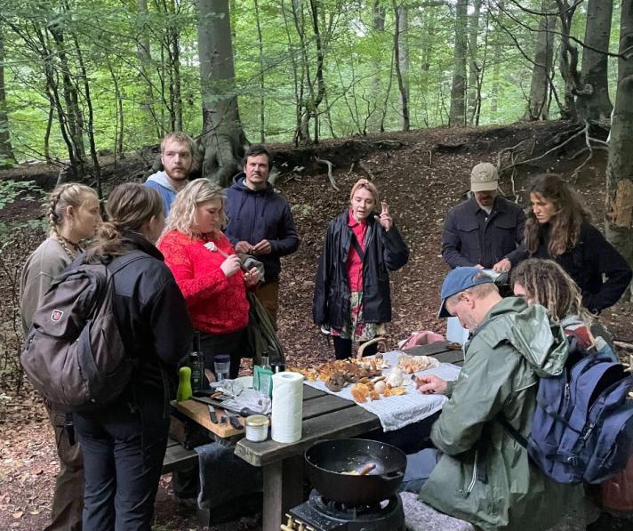 A woman provides information on mushrooms to a group of people in a forest