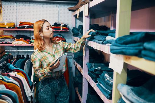 Young woman looking for clothes on cloth shelf