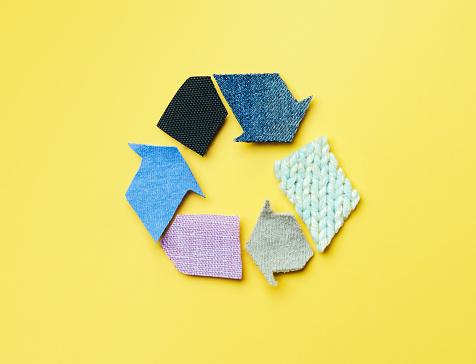 Yellow background with recycling symbol made of textiles.