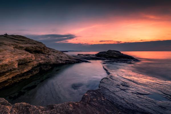 Sunset landscape depicting body of water and rocky cliff.