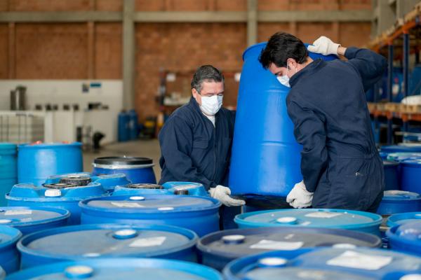 Men working at a chemical plant carrying barrels with toxic products